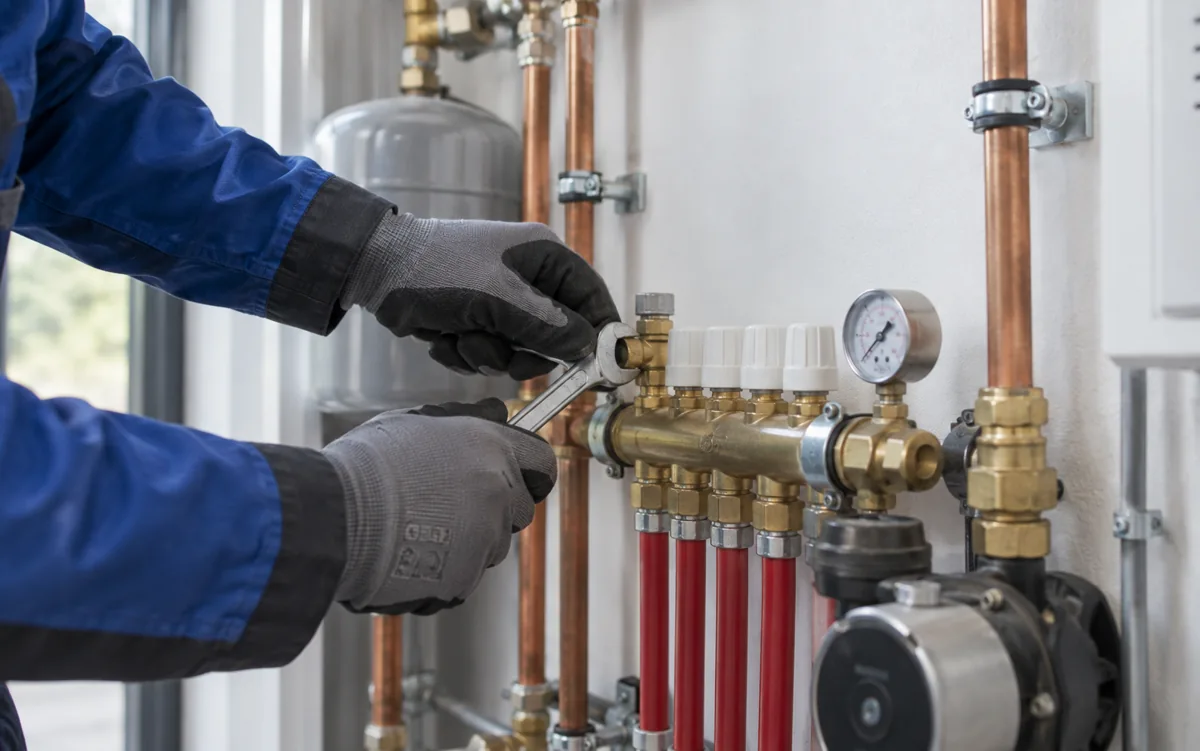 Installateur werkt met een steeksleutel aan een verwarmingsverdeler.